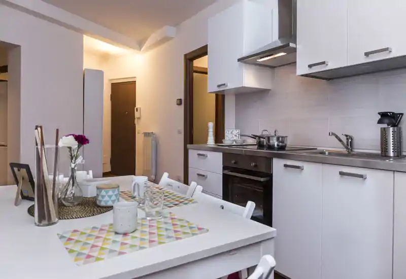Cuisine moderne équipée avec meubles blancs, four encastré et une table dressée avec des sets et de petites décorations — lumineuse, soignée et prête à être utilisée.