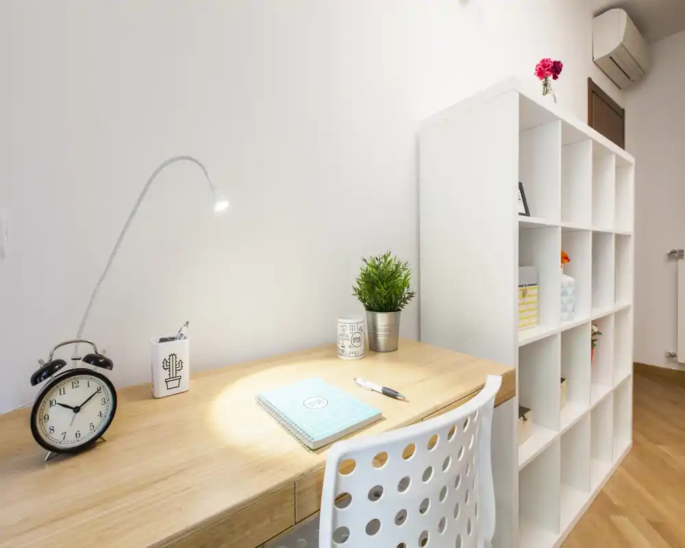 Espace bureau moderne et lumineux dans une pièce à vivre, avec plateau en bois, lampe de travail, petite plante et étagères — idéal pour étudier ou télétravailler.