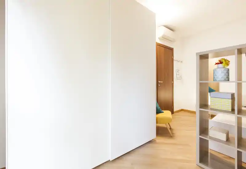 Angolo della camera luminoso e minimale con un grande armadio bianco, scaffalatura a cubi e una piccola poltrona gialla — perfetto per mettere in risalto gli spazi di stoccaggio e l’arredo fresco.