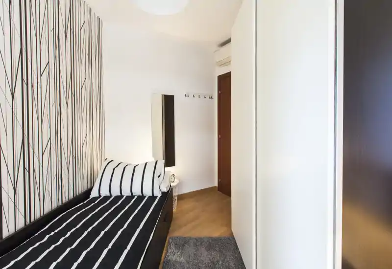 Habitación individual compacta con cama a rayas y pared decorativa moderna; espacio luminoso y bien ambientado, ideal para estancias cortas.