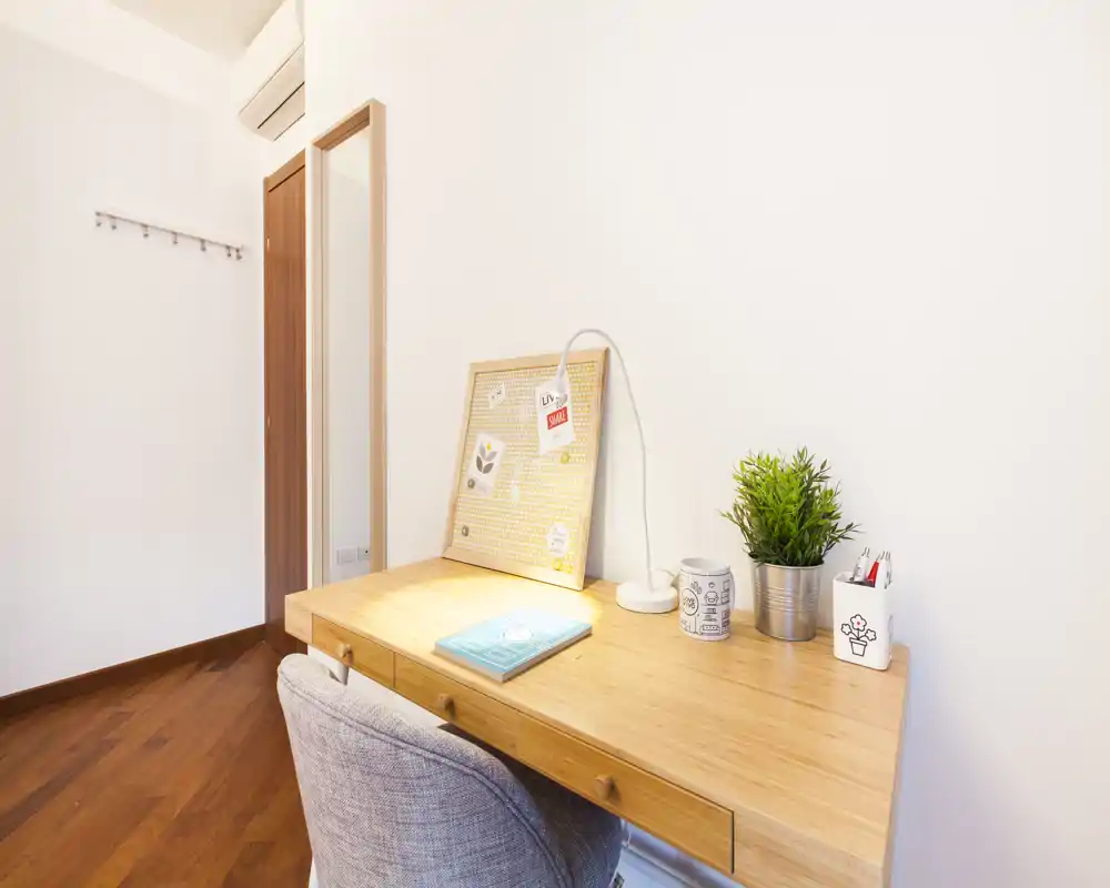 Angolo studio luminoso e minimale con scrivania in legno, lampada, bacheca e pianta: ideale per studiare o lavorare da remoto in un appartamento compatto.