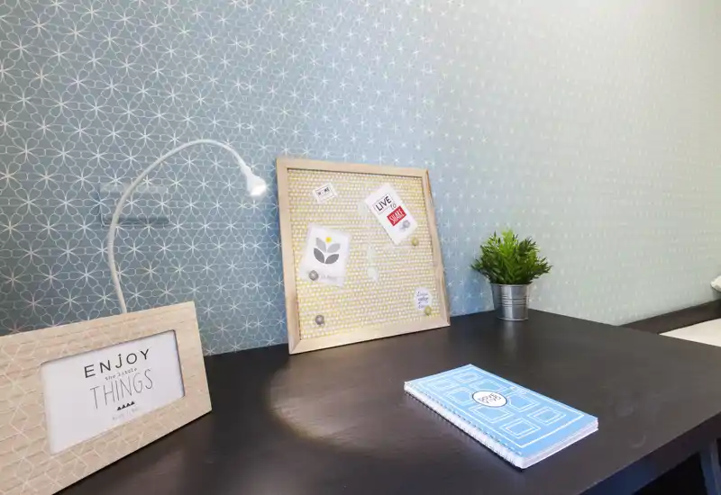 A close-up of a bedside/desk surface with a decorative lamp, framed note board, small plant and notebook — a styled vignette suitable for lifestyle shots near a bed.