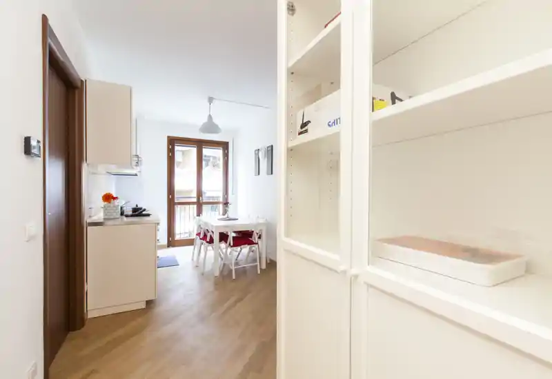 Bright, compact dining area with a small table and chairs next to a kitchenette and balcony door — ideal for a cozy two-person meal.