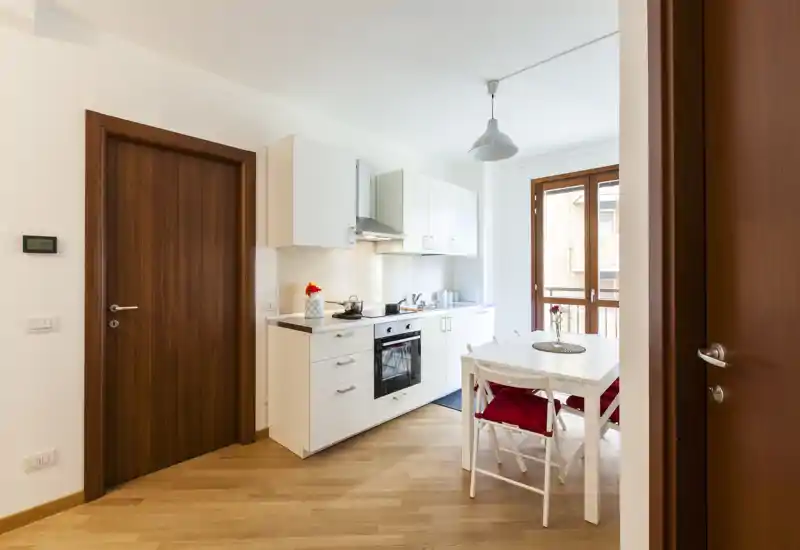 Bright, modern open kitchen with white cabinets, built-in oven and a small dining table by the window — cozy and well lit for a compact apartment.