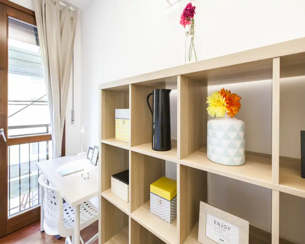 Zona giorno luminosa e ben arredata con una libreria a cubi e una scrivania vicino alla finestra — moderna, ariosa e ideale per lavorare o rilassarsi.