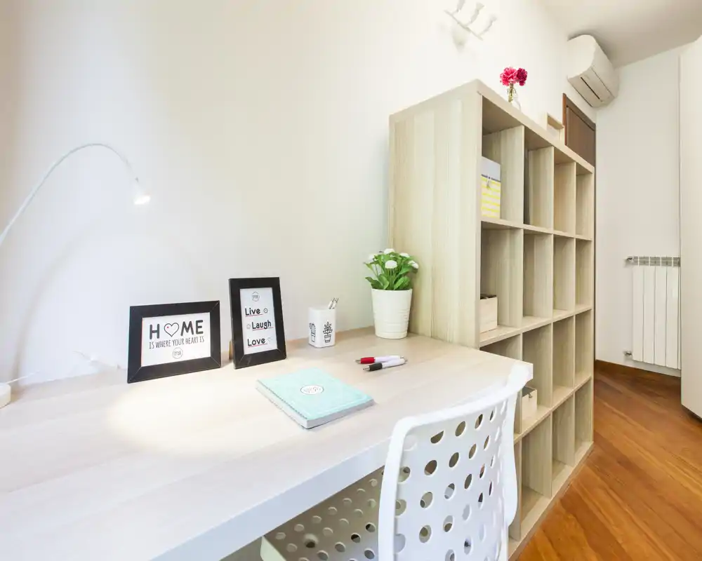Angolo living/lavoro luminoso e moderno con scrivania ordinata, scaffalatura e dettagli decorativi; ideale per uno spazio di lavoro compatto in appartamento.
