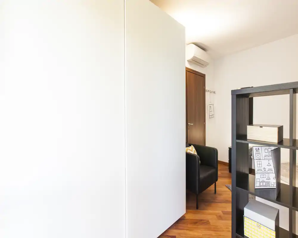 Bright, compact living area with a modern armchair, wooden floors and open shelving creating a functional, cozy corner.