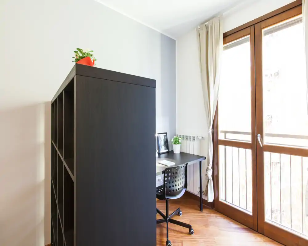 Bright living area with a compact home-office corner: a desk, chair and shelving near large glazed doors offering abundant natural light.