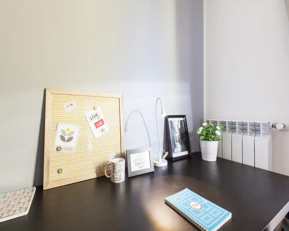 A tidy bedroom desk corner with a pinboard, framed photos, a desk lamp and a small plant on a dark wood surface — ideal for work or study.