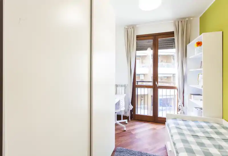 Habitación individual luminosa y acogedora con puerta balcón, suelo de madera y estantería; ideal para estudiante o una persona.