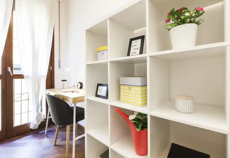 Coin séjour moderne et lumineux avec une étagère décorative, un bureau et la lumière naturelle d'une grande fenêtre — un espace cosy et bien aménagé, idéal pour travailler ou se détendre.