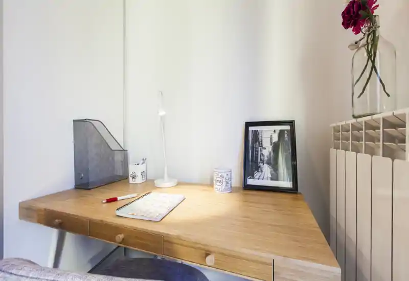 Rincón luminoso y minimalista entre sala y área de trabajo con escritorio de madera, lámpara, foto enmarcada y pequeños objetos decorativos — perfecto como puesto compacto.