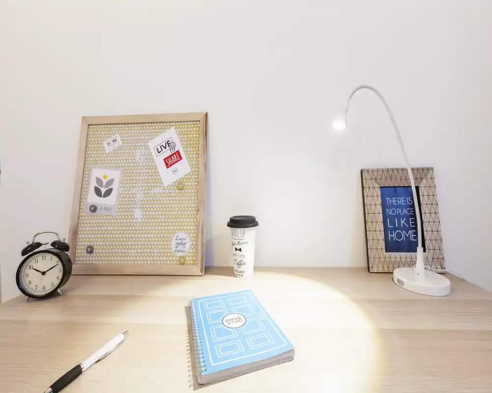 Rincón de escritorio luminoso y minimalista con cuaderno, lámpara, despertador y marcos decorativos: un pequeño espacio de trabajo ordenado y acogedor.