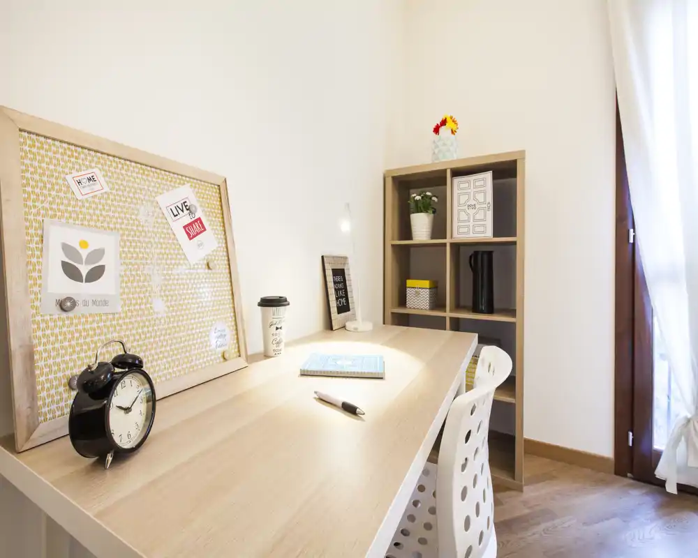 Rincón de trabajo luminoso y ordenado con escritorio de madera, silla, estantería y lámpara de mesa — ideal para estudiar o trabajar.