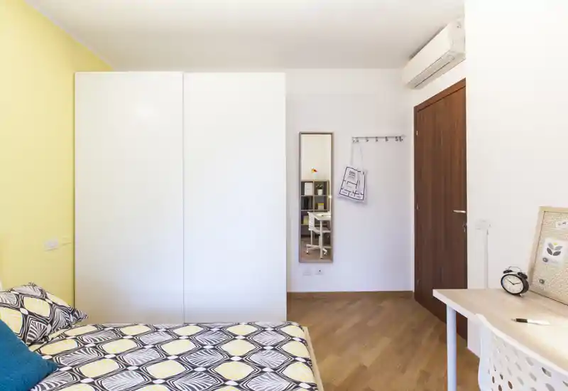 Dormitorio moderno y luminoso con ropa de cama estampada, gran armario blanco, mesa de estudio y espejo de cuerpo entero — estilo limpio y suelo de madera cálido que lo hace acogedor.