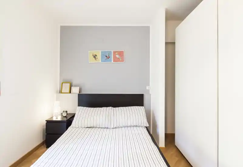Camera da letto luminosa e minimal con letto matrimoniale ben rifatto, lenzuola a righe, comodino e piccoli dettagli decorativi — pulita, moderna e accogliente.