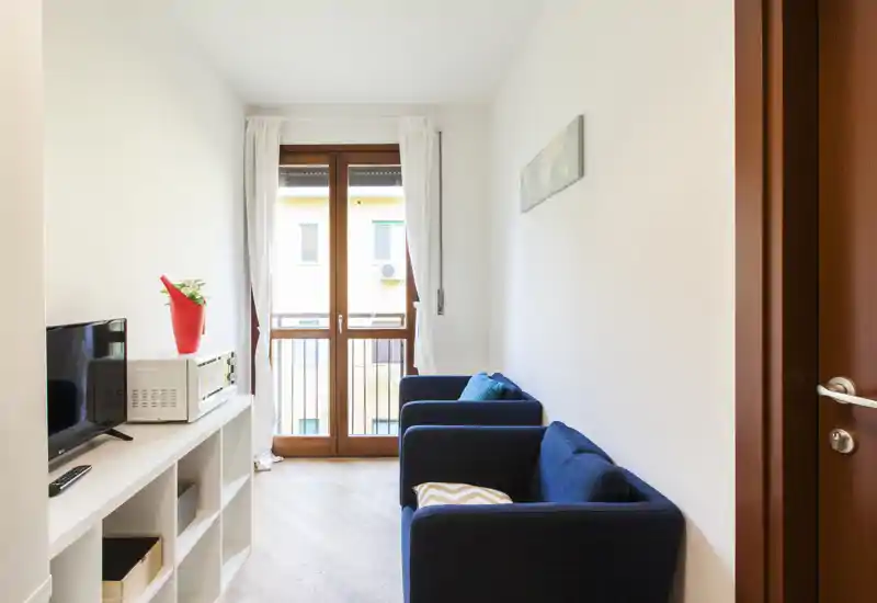 Espace séjour compact et lumineux avec deux fauteuils bleu marine, un meuble TV et une porte-fenêtre donnant sur un balcon, parfait pour se détendre dans un petit appartement.