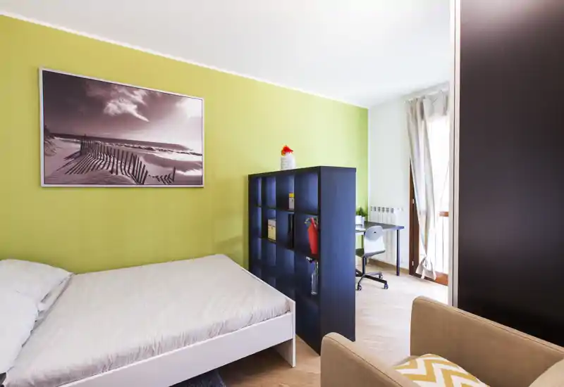 Bright, modern bedroom with a large bed, decorative shelving divider and natural light from a balcony window — minimal, fresh styling ideal for a short-term rental.
