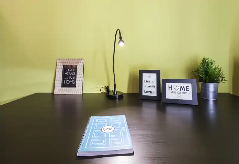 Coin bureau soigné avec une petite lampe, des cadres décoratifs et une plante en pot — idéal pour un espace de travail à domicile compact.