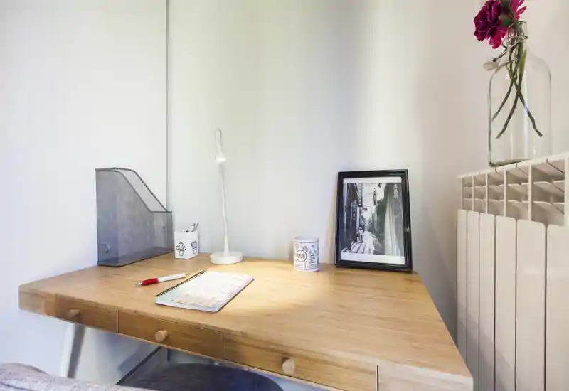 Rincón de oficina en casa luminoso y minimalista con escritorio de madera, lámpara pequeña, material de oficina y foto enmarcada — un espacio de trabajo ordenado para concentrarse.