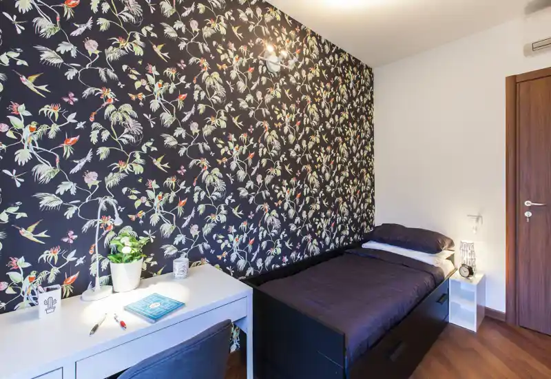 Habitación individual compacta y con estilo con pared estampada, ropa de cama oscura y un escritorio ordenado. Buena iluminación y decoración cuidada, ideal para estudiante o una persona sola.
