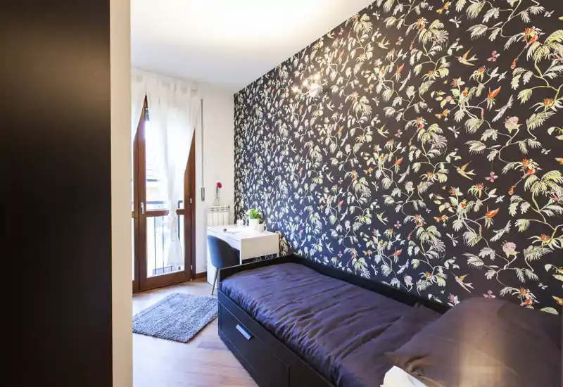 Dormitorio individual luminoso y con estilo, pared decorativa, cama cómoda, escritorio y acceso al balcón — ideal para una estancia acogedora.