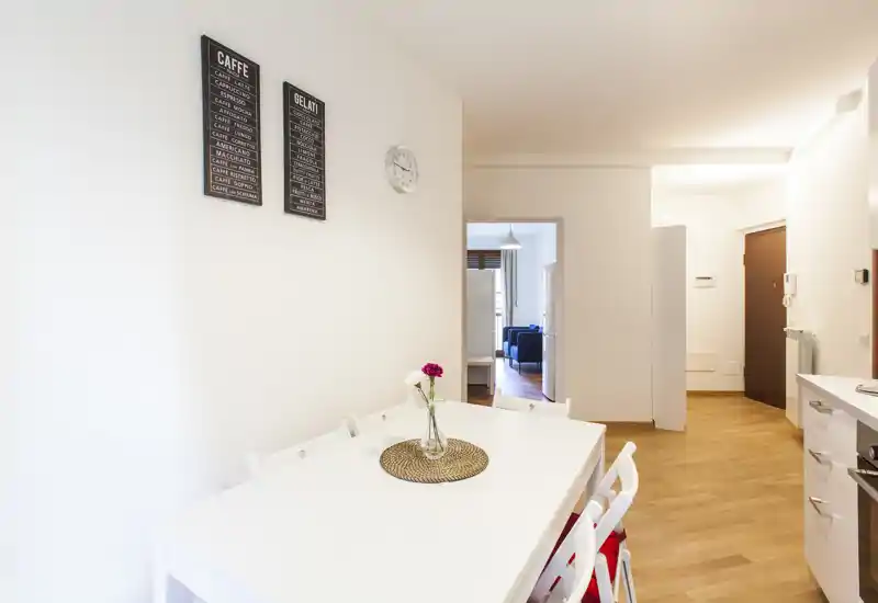 Coin repas lumineux et minimaliste avec table et chaises blanches, vase décoratif au centre et sol en bois chaleureux — idéal pour appartements compacts.