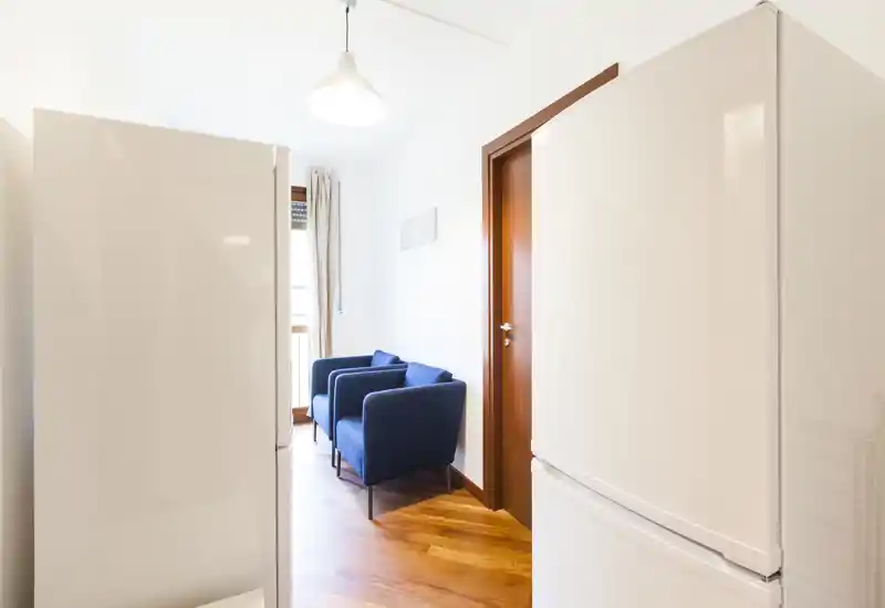 Espace séjour lumineux et minimaliste avec deux fauteuils bleus près de la fenêtre ; parquet en bois et murs blancs pour une atmosphère aérée.