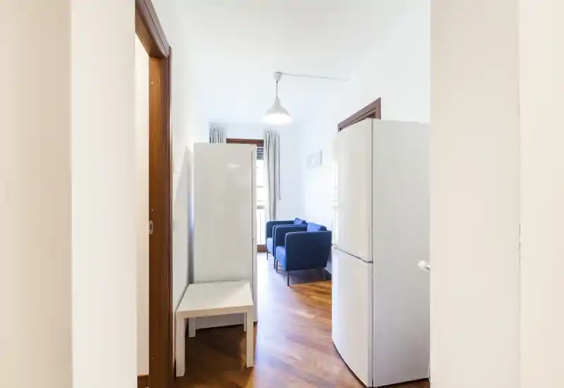 Espace de vie compact vu depuis le couloir : deux fauteuils bleus sur un sol en bois chaleureux, éclairés par la lumière naturelle de la fenêtre. Parfait pour un coin salon cosy dans un petit appartement.