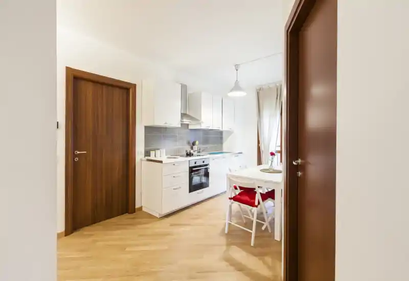 Cuisine compacte et lumineuse avec meubles blancs, four encastré et petite table avec coussins rouges — idéale pour un appartement de ville chaleureux.