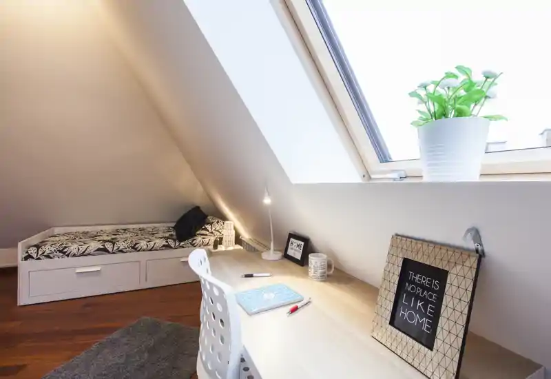 Camera mansardata compatta con letto singolo a giorno, finestra a tetto luminosa e scrivania in legno ordinata — accogliente, ben illuminata e adatta allo studio o al relax.
