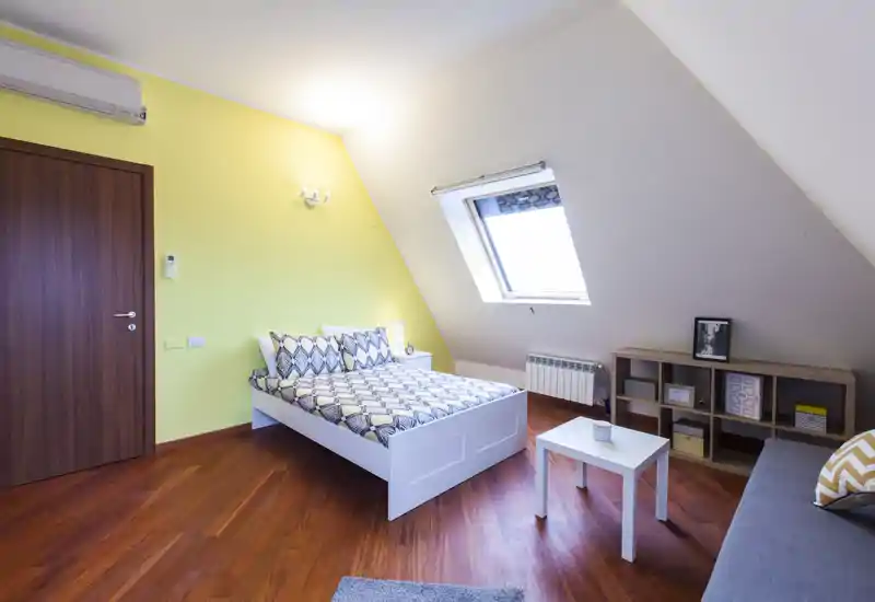 Camera da letto mansardata, luminosa e moderna con letto matrimoniale, biancheria a motivo e una finestra a tetto che illumina l’ambiente. Pavimento in legno caldo, mobile a cubi e arredo minimal per un soggiorno accogliente.