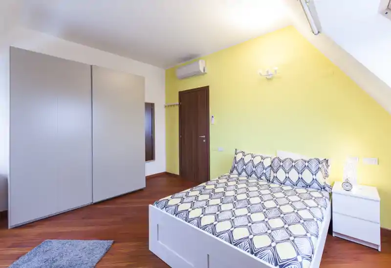 Camera da letto moderna e luminosa con letto matrimoniale con stampa geometrica, comodino e armadio; pavimenti in legno caldo e parete gialla creano un ambiente accogliente.
