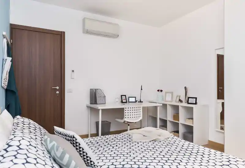 Dormitorio moderno y ordenado con ropa de cama estampada, escritorio compacto y estanterías—luminoso, bien decorado y listo para huéspedes.