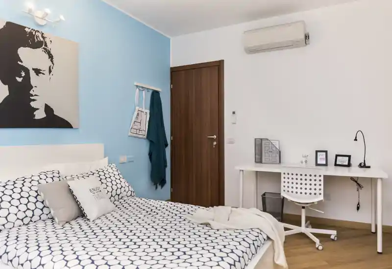Dormitorio moderno y luminoso con cama doble vestida con ropa de cama estampada, un escritorio pequeño y pared azul que aporta calma — ideal para una estancia cómoda.