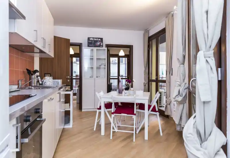 Bright, modern open kitchen with a small dining table set for four. White cabinets, wooden floors and large windows create an airy, welcoming space ideal for city stays.