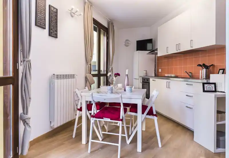 Bright, compact open kitchenette with a small dining table and four cushioned chairs, modern white cabinets and orange tile backsplash—ideal for cosy city stays.