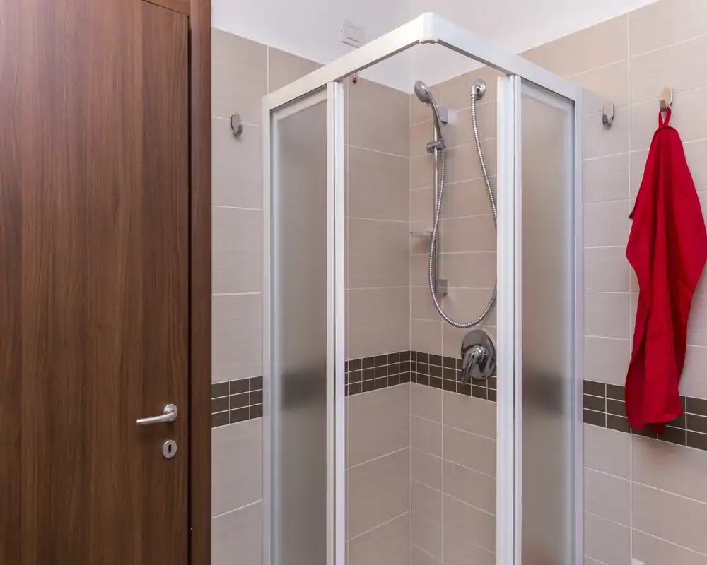 Bagno compatto e moderno con box doccia angolare, doccetta e pareti piastrellate; luminoso, pulito e ben tenuto.