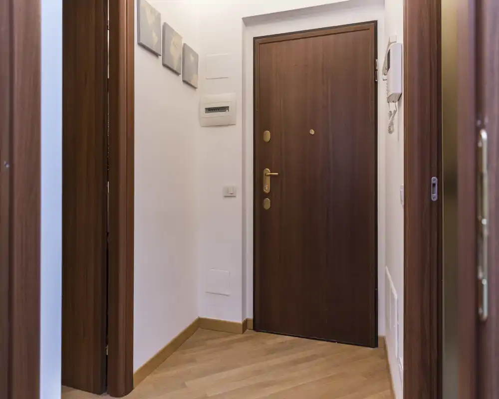 Ingresso piccolo e luminoso con porta d'ingresso in legno, pavimento in parquet e pareti bianche pulite — ottimo impatto per un annuncio.