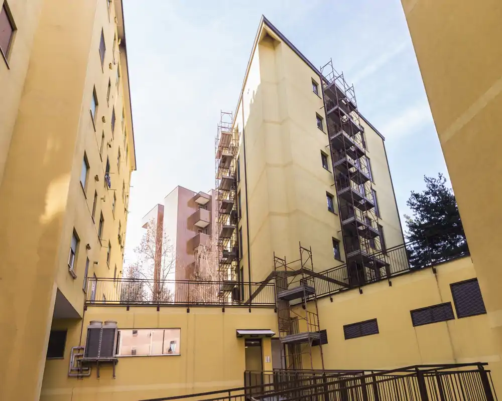 Cortile soleggiato del condominio con facciate esterne, impalcature e passerelle — adatto a mostrare lo stato dell’edificio e gli accessi esterni.