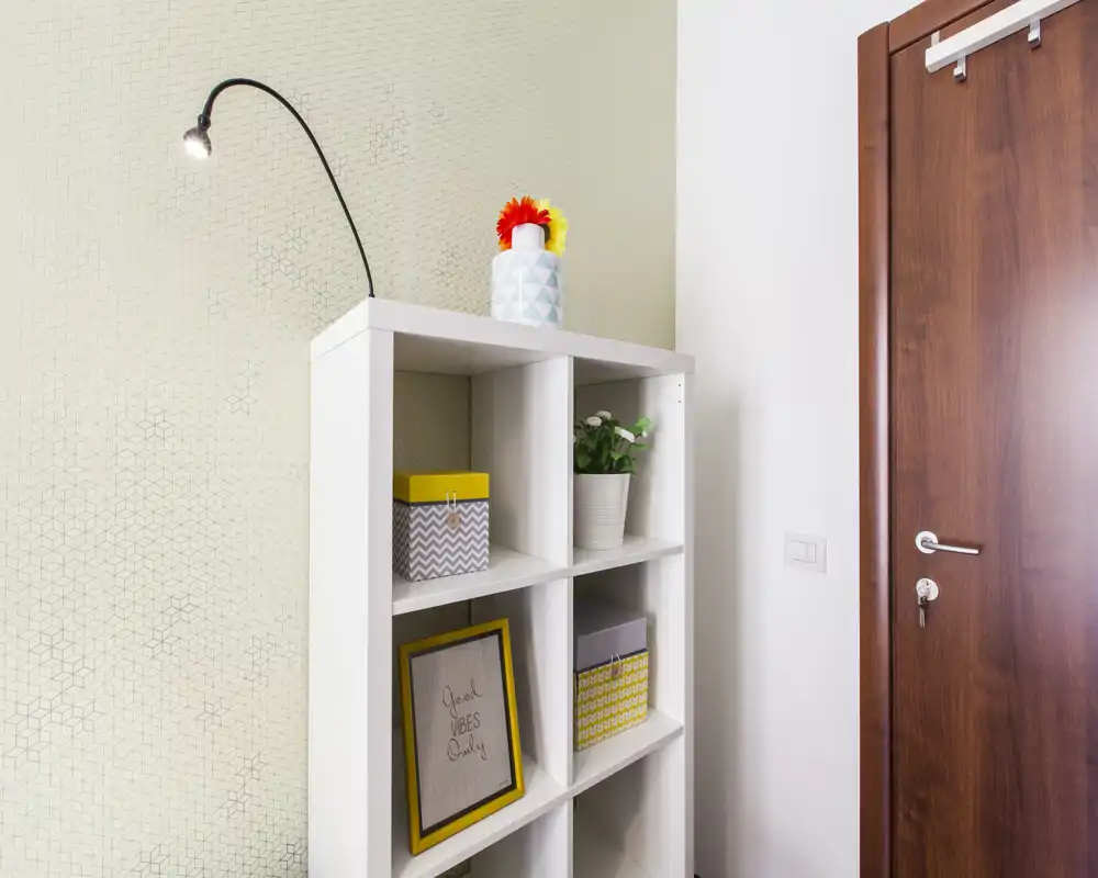 Ingresso ordinato con scaffale bianco a cubi, scatole decorative e porta in legno; spazio luminoso e curato perfetto per una buona prima impressione.