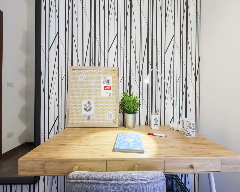 Rincón de trabajo luminoso y moderno con escritorio de madera, lámpara de escritorio, pequeña planta y panel de corcho — un área de estudio impecable ideal para anuncios de alquiler.