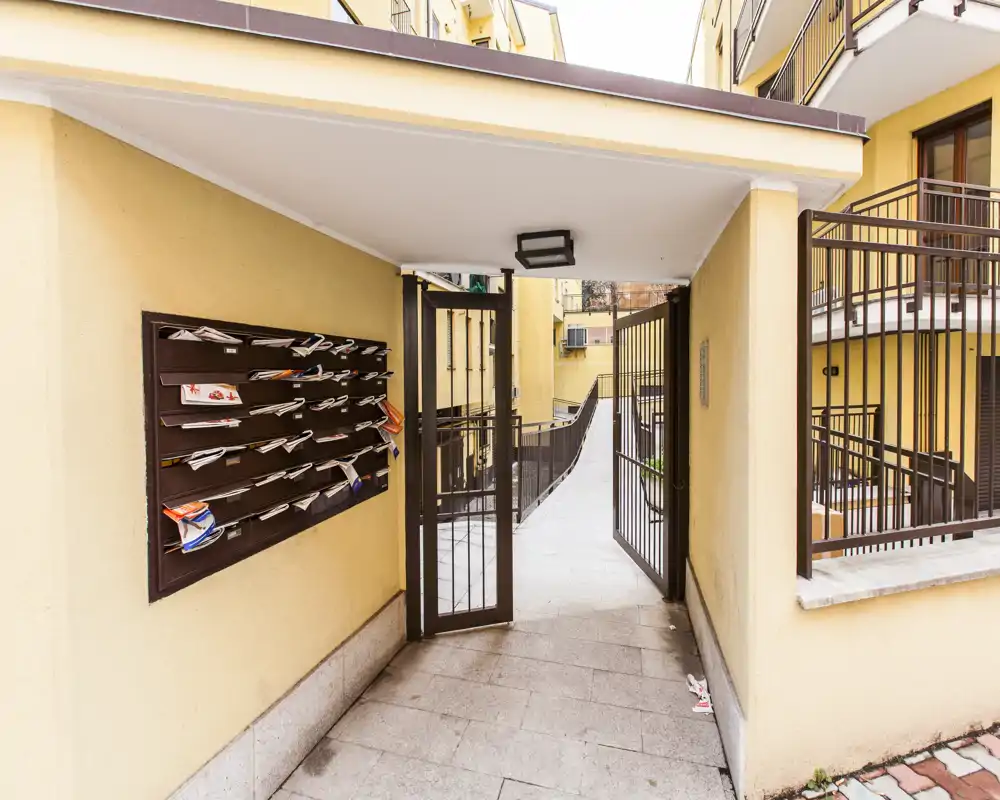 Atrio d'ingresso condominiale con cassette postali, cancello d'accesso e rampa interna — luminoso e ben curato.
