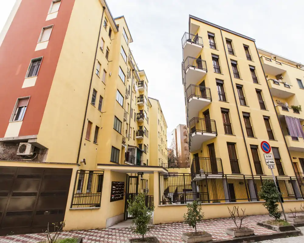Vista esterna di un edificio residenziale con cortile recintato, balconi e marciapiede lastricato; adatta a mostrare la facciata e l'accesso principale.
