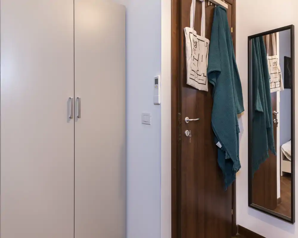 Entrada compacta y ordenada con armario cerrado, espejo de cuerpo entero y perchas en la puerta para abrigos y bolsos — práctica para el día a día.