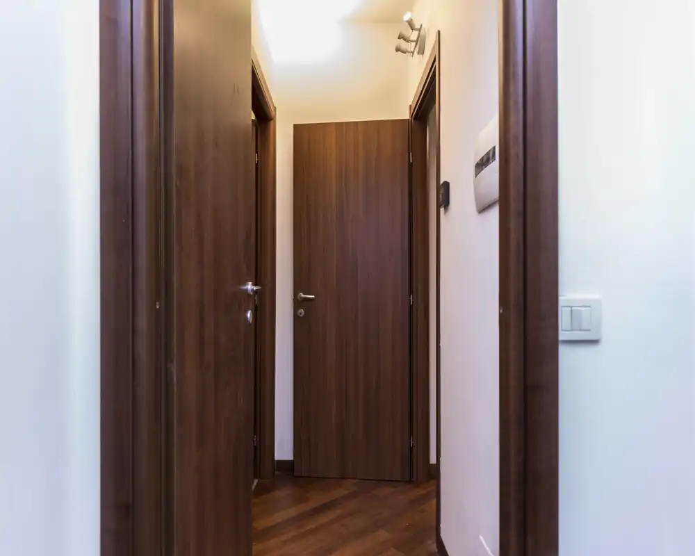 Pasillo sencillo y bien iluminado del apartamento con puertas de madera cerradas y suelo de parquet: área de entrada/neutra adecuada para mostrar el acceso a las habitaciones.