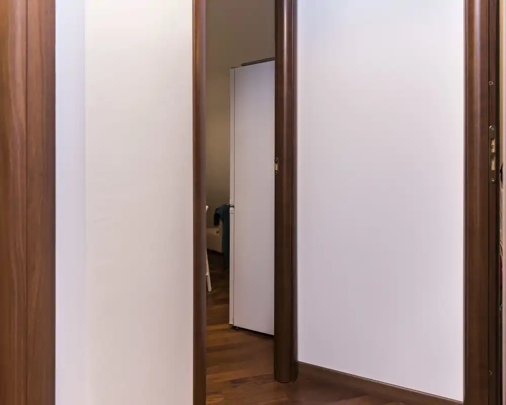 Entrada/pasillo interior estrecho con marcos de madera y suelo de parquet; vista hacia una habitación contigua. Pasillo limpio y minimalista, útil para destacar la circulación en el anuncio.