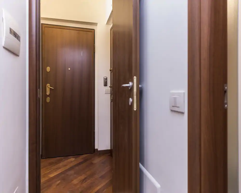 Pequeño recibidor con puerta de madera, suelo de parquet y paredes neutras. Imagen limpia y bien iluminada, adecuada para un anuncio.