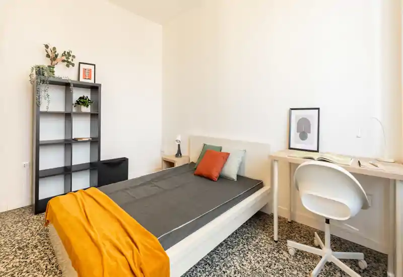 Camera da letto luminosa e minimalista con letto singolo, comodino, libreria a cubi e una scrivania piccola — ideale per uno studente o una persona sola. Linee pulite, luce naturale e dettagli decorativi come cuscini e plaid.