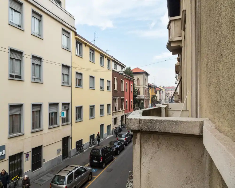 Vista dal balcone sulla strada: una via cittadina stretta con auto parcheggiate e palazzi vicini; utile per mostrare l’affaccio esterno e il contesto urbano.